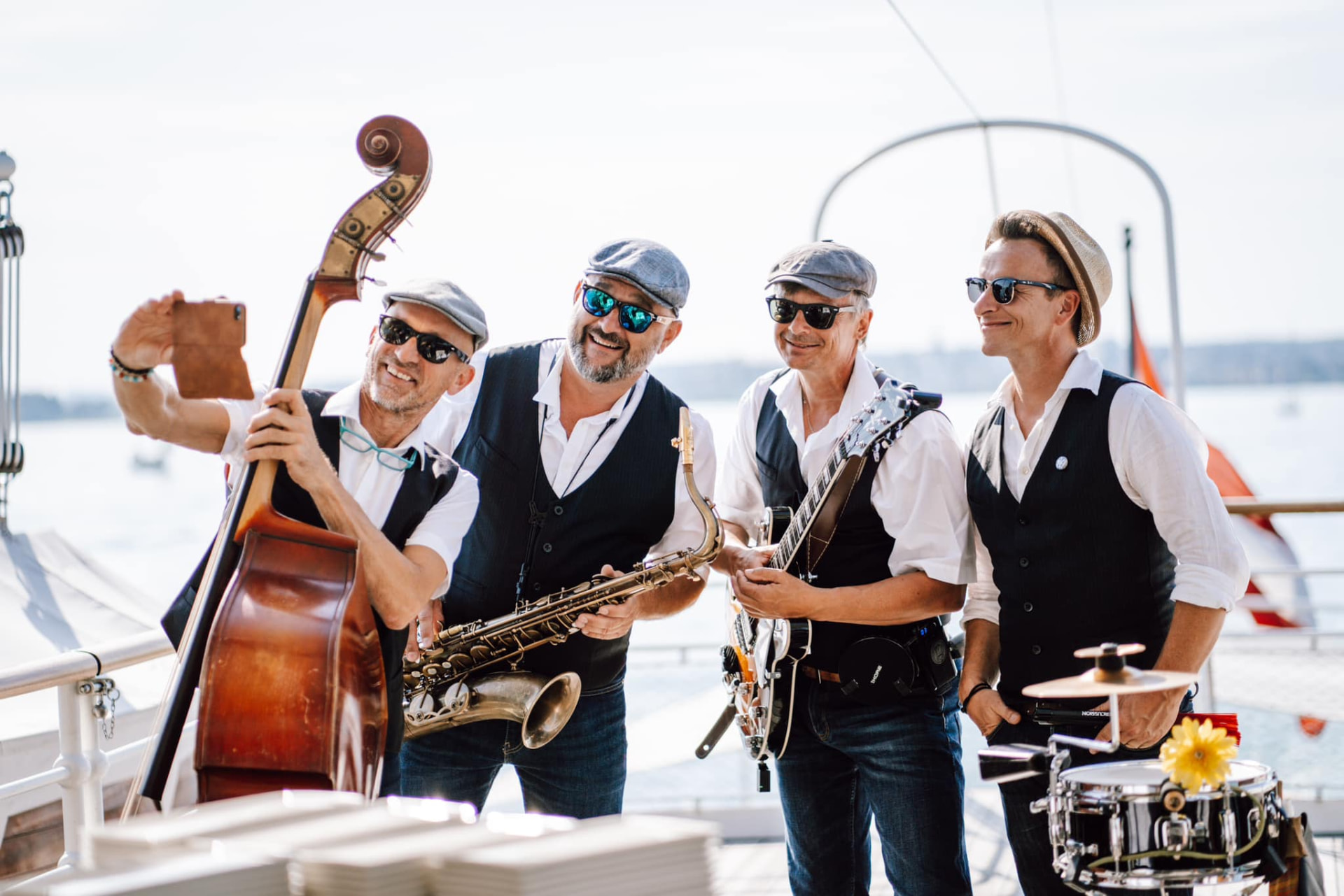 The Swingbugs machen ein Selfie mit Kontrabass, Saxofon, Gitarre und Schlagzeug an Deck eines Schiffes